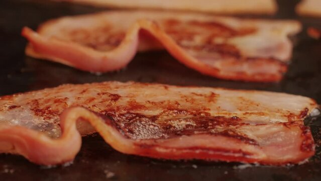 Cooking bacon slice for burgers on the grill close-up macro. The chef in kitchen of the restaurant making cutlets for smash burgers - smash burger beefsteak. Fast and street