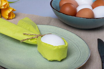 Happy Easter! Easter egg in bunny napkin on plate with cutlery, bunny, spring flowers.  Top view. Stylish Easter brunch.