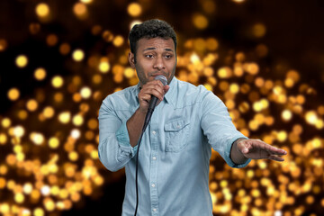 Male performer talking into microphone on festive bokeh background. People, entertainment and holiday concept.