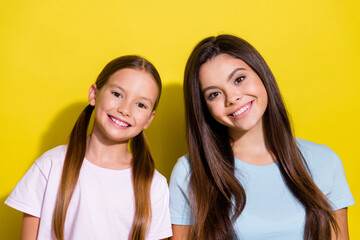 Photo of cheerful good mood little sisters wear t-shirts smiling isolated yellow color background