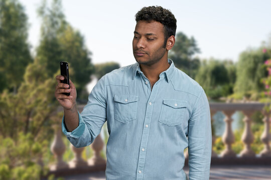 Young confident man taking picture with his smartphone standing outdoors. People, technology and lifestyle concept.