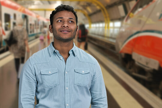 Young pensive man standing daydreaming on blur train station background. Portrait of young thoughtful man.