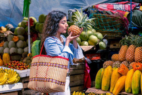 Latin girl in the middle of a fresh fruit market, with a basket holding a pineapple in her hands.