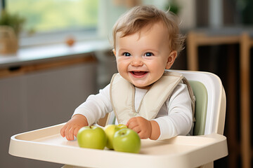 Fototapeta premium happy little cute smiling baby sitting at white high chair with green apples