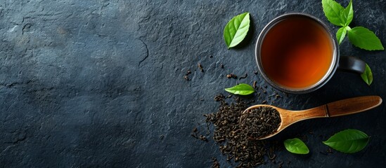 Black tea cup and wooden spoon with tea leaves on rustic table with space for text. - obrazy, fototapety, plakaty