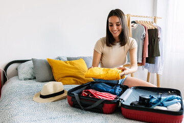 Happy young woman preparing luggage before summer travel vacation or weekend getaway. Packing...