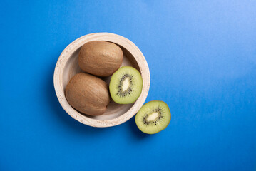 Kiwi fruit in a wooden bowl on a bright blue background. One sliced in half.