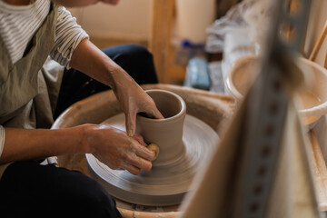 An artist shapes a clay pot with precise movements on a spinning pottery wheel.