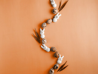 Creative Easter wave composition made from motley quail eggs, marshmallow bunny and grass on peach...