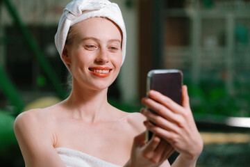 Portrait of close up beautiful caucasian woman in white towel taking video of calm and relaxing nature by using her mobile phone. Pretty girl with beautiful skin take photo. A Side view. Tranquility.