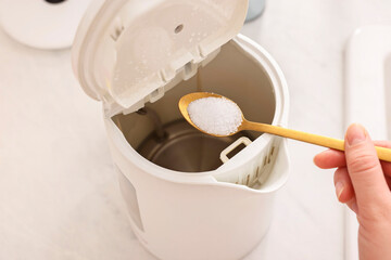 Cleaning electric kettle. Woman adding baking soda to appliance at table, above view