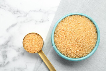 Brown sugar in bowl and scoop on white marble table, top view