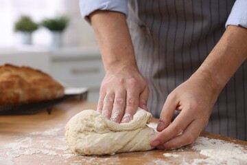Making bread. Man kneading dough at wooden table in kitchen, closeup