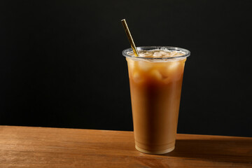 Refreshing iced coffee with milk in takeaway cup on wooden table against black background, space...