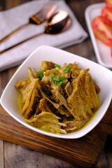 Tengkleng Kambing is is a traditional Central Javanese dish made from young goat bones, with spices, soy sauce, chili. served in a white ceramic bowl on a brown wooden table. Indonesian food. 