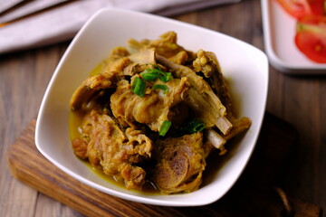 Tengkleng Kambing is is a traditional Central Javanese dish made from young goat bones, with spices, soy sauce, chili. served in a white ceramic bowl on a brown wooden table. Indonesian food. 