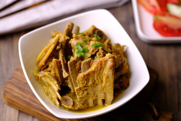 Tengkleng Kambing is a traditional Central Javanese dish made from young goat bones, with spices, soy sauce, chili. served in a white ceramic bowl on a brown wooden table. Indonesian food. 