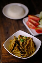 Tengkleng Kambing is is a traditional Central Javanese dish made from young goat bones, with spices, soy sauce, chili. served in a white ceramic bowl on a brown wooden table. Indonesian food. 