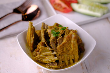 Tengkleng Kambing is a traditional Central Javanese dish made from young goat bones, with spices, soy sauce, chili. served in a white ceramic bowl on white wooden table. Indonesian food. 