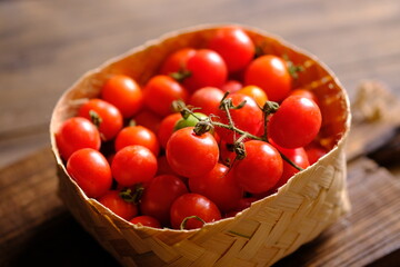 fresh cherry tomatoes in a bamboo basket on a brown wooden rustic table. Contains vitamins C, A, lycopene. Solanum lycopersicum var. cerasiforme. Cherry tomato. Tomat Ceri. 
