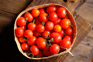 fresh cherry tomatoes in a bamboo basket on a brown wooden rustic table. Contains vitamins C, A, lycopene. Solanum lycopersicum var. cerasiforme. Cherry tomato. Tomat Ceri. 
