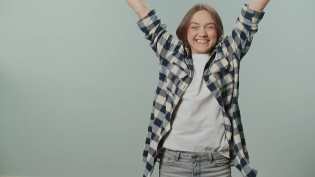A Portrait of a Happy Young Woman in Yellow Gloves,Holding a Cleaning Spray Bottle and Rag, Rejoices at the Success in Cleaning, Jumps for Joy on the Gray Background.Decluttering Hacks.
