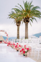 Bright bouquets of flowers stand along rows of white chairs in front of the wedding arch