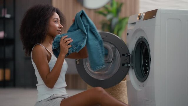 African American woman housewife sad upset shocked biracial ethnic girl pull out of washing machine laundry take jeans find broken wet smartphone forgot mobile phone in cloth pocket waterproof gadget