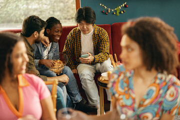Group of smiling male friends is talking and looking on phone during festive home party