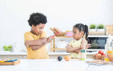 Obraz na płótnie Canvas Angry african brother and little sister madly looking at each other with arms crossed gesture while playing toys together at home kitchen. Siblings children conflict concept