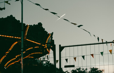 Carousel merry-go-round silhouette, triangles string garland against evening sky Fairyland,...