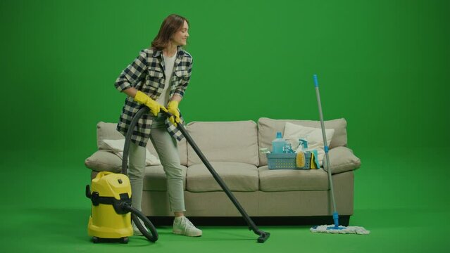 Green Screen.A Smiling Young Woman Housewife in Yellow Rubber Gloves is Vacuuming Near the Couch. Smart Cleaning Technology. Eco-friendly Cleaning with Appliances.