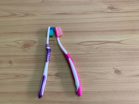 toothbrush on the table, Two toothbrushes pink and purple lying on a wooden surface