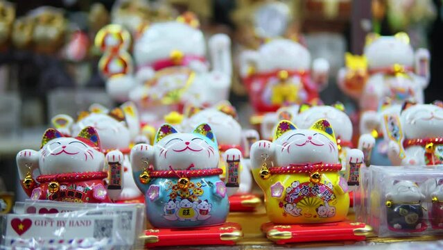 Storefront with variety of traditional Chinese souvenirs in form of cat with moving paw filmed in closeup. Lots of Maneki Neko funny statues usually bought as souvenirs are put in a row on shop window