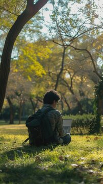 There is a man sitting in the grass with a laptop