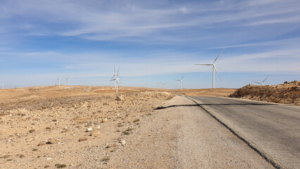 A remote desert road passing through wind turbine farm producing renewable energy in remote location of Jordan, Middle East 