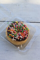 Chocolate topping donuts and colorful sprinkles in mica plastic on a wooden table