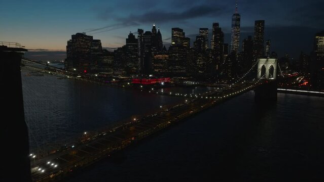 alt sunset view of downtown NYC flying backwards alongside illuminated Brooklyn Bridge