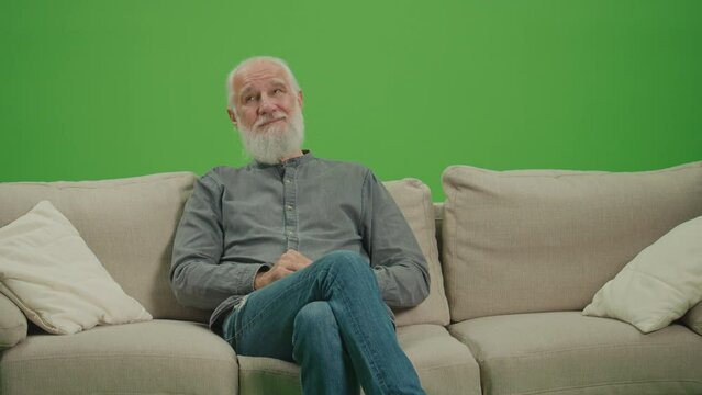 Green Screen. Relaxed Old Man with a Gray Beard Resting Sitting on Sofa. The Concept Of Enjoying Life In Retirement. Pension Provision.