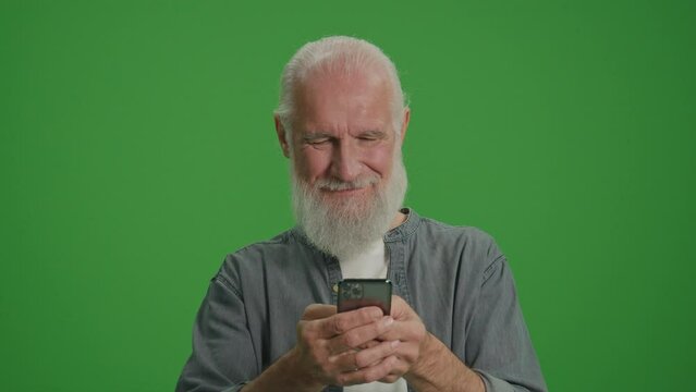 Green Screen.A Smiling Old Man with Gray Beard Scrolls on the Phone. Happy Elderly Man Shops Online. Assistive Technology for Seniors. Smart Homes and Aging in Place.