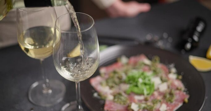 Woman pours white win onto glass to complement dinner with tuna carpaccio