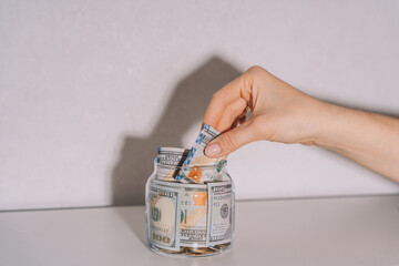A hand takes dollar bills from a glass jar.