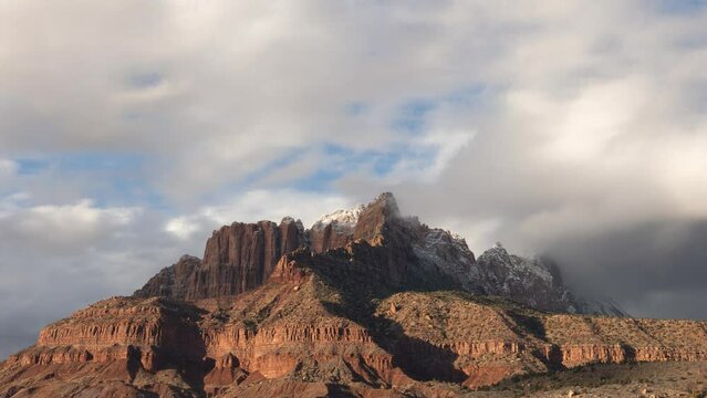 4k time lapse video of low winter clouds drifting over Mt. Kinesava in Zion Nat. Park, Utah, USA as sun gradually sets painting the cliffs brilliant orange and the clouds pink before fading to blue