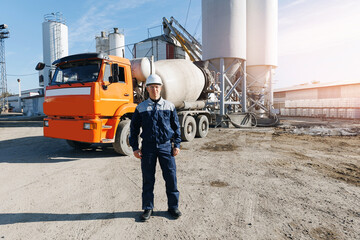 Portrait happy worker of concrete factory, young man in uniform with hard hat on background cement...