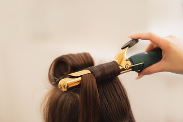 Stylist skillfully curling hair with golden iron in salon, hairstyle for wedding