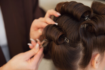 Stylist skillfully curling hair with golden iron in salon, hairstyle for wedding