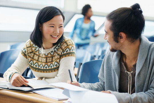 Conversation, university and students in classroom for studying with textbook for test or exam. Discussion, writing and young people working on college assignment together in lecture hall at academy