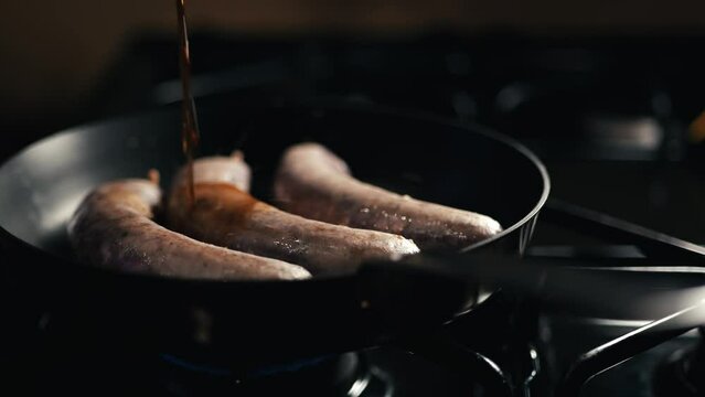 Three sausages cooking on a skillet on a stovetop 