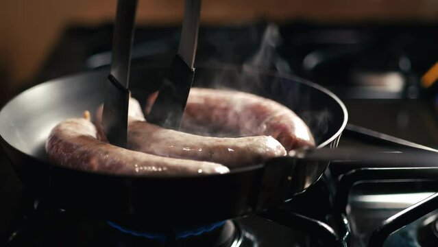 Three sausages cooking on a skillet on a stovetop 