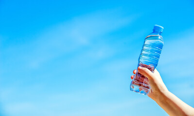 A girl holds a bottle of drinking water in her hand against a blue sky background
